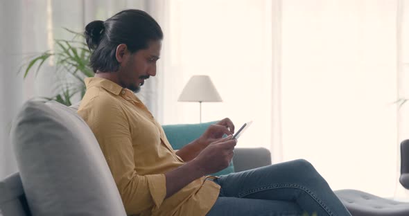 Handsome man sitting on the couch at home and connecting with a digital tablet