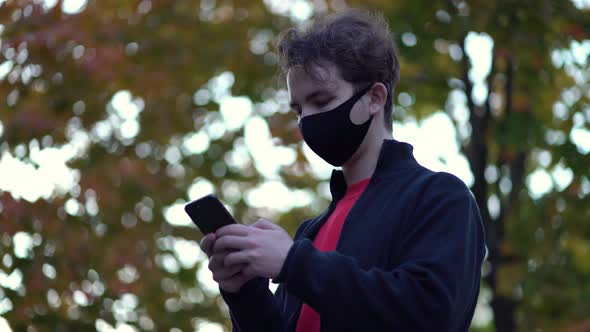 Portrait Boy in Protective Medical Mask Walks Down To the Street Uses Phone Texts Scrolls Surfs the alt