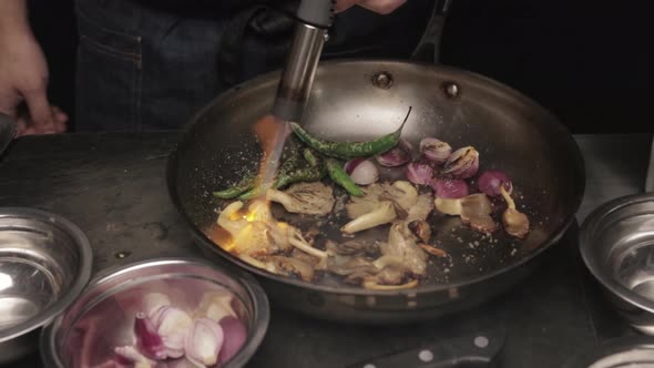 Chef Charring Vegetables In Pan With Blowtorch, close up alt