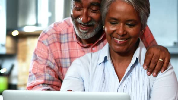 Senior couple using laptop in the kitchen alt
