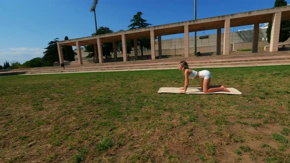 Girl in White Dress Doing Stretching Exercises on the Grass at Sunny Day