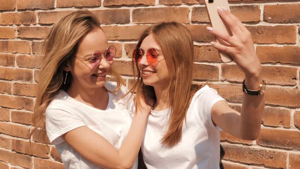 Two young beautiful blond smiling hipster girls in trendy summer clothes alt