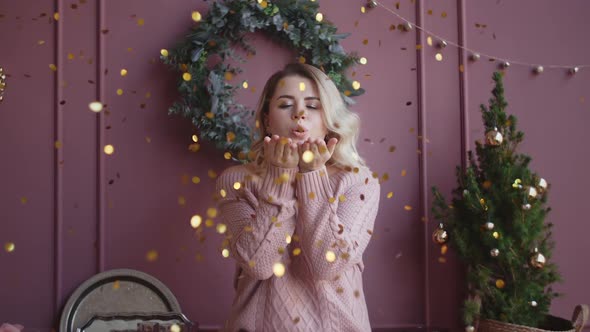 Beautiful Woman in Sweater Blows Shiny Confetti From Her Hands To the Camera in Slow Motion alt