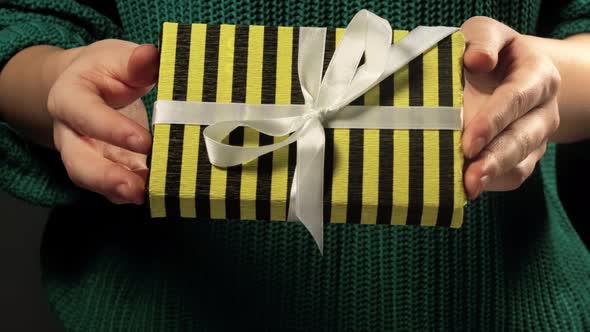 Girl  hand holding a gift wrapped in striped black yellow paper tied with white ribbon