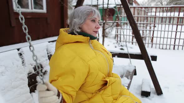 Adult Woman Sways on a Swing and Looks Alone Into the Distance Around the Snow