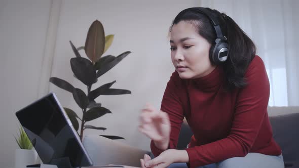 Freelance woman redshirt using tablet with headphone for meeting online at home alt
