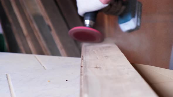 Male artisan polishes a wooden board using a grinding machine in a workshop