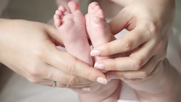 Close Up of Female Hands Hold and Caress Little Cute Feet of Newborn Baby alt