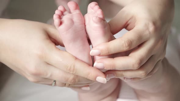 Close Up of Female Hands Hold and Caress Little Cute Feet of Newborn Baby