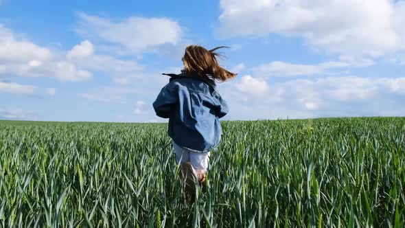 A Teenage Girl in Denim Clothes Runs Across a Wide Green Field alt