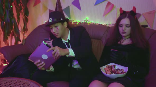 A Guy in a Creepy Costume is Actively Playing on a Tablet and the Girls are Sitting on the Phone at alt