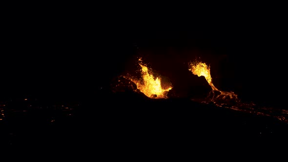 Aerial flying over an active volcano as lava spews into the dark night. alt
