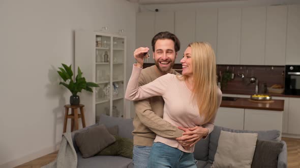 Happy Caucasian Family Couple Showing New House Keys to Camera While Posing Indoors alt