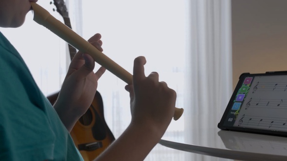 Joven practica tocar flauta dulce con una App en su habitación solo