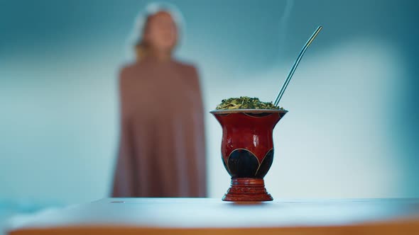 Young Woman Covers Herself with Blanket and Takes Traditional Hot Mate Drink From the Table alt