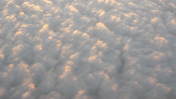 Airplane window view of clouds floating in the sky below the aircraft alt