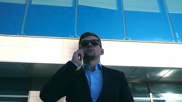 Portrait of Young Businessman in Sunglasses Talking on Phone Outdoor Near Office alt