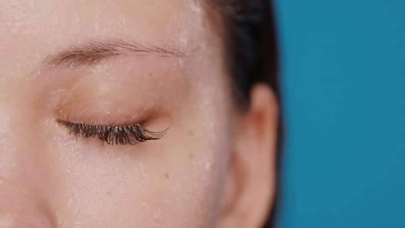 Close-up of Closed Woman Eye Getting Water Splashes Isolated on Blue alt