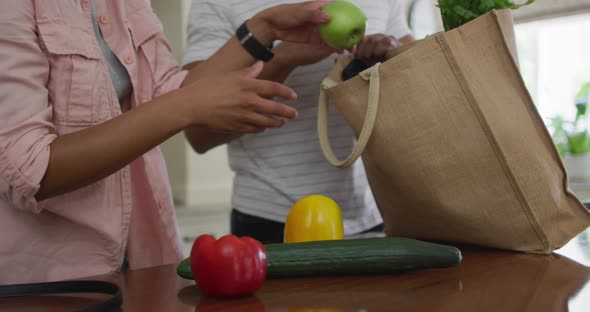 Hands of biracial couple unpacking groceries in kitchen alt