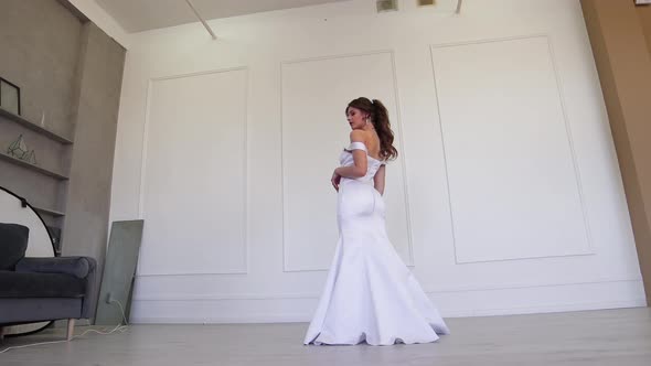 A Girl in a Wedding Dress Poses for the Photographer with Her Back Turned alt