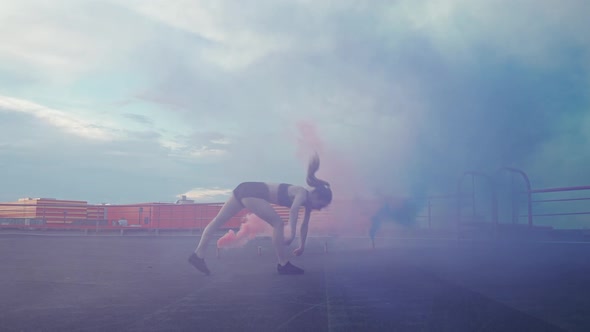 Slow Motion Female Gymnast Doing a Flip Somersault in a Smoky Space Multi Colored and Blue Smoke alt
