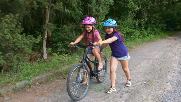 Two girls in protective bicycle helmets in the summer in the park. The older sister helps