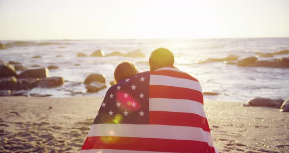 Couple wrapped in American flag sitting on the beach 4k