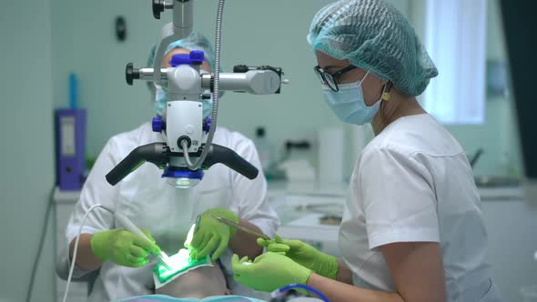 Side View Professional Dental Assistant Passing Instruments to Doctor at Dental Microscope in Slow alt