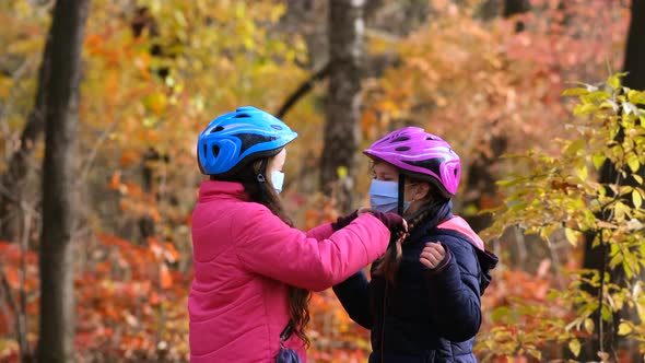The older sister puts on the younger one a medical mask and a Bicycle safety helmet in the fall