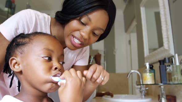 Mother teaching her daughter to brush her teeth in bathroom 4k alt
