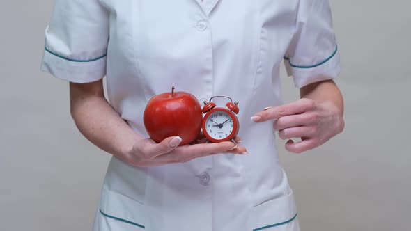 Nutritionist Doctor Healthy Lifestyle Concept - Holding Organic Red Apple and Alarm Clock alt