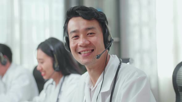 Close Up Of An Asian Man Doctor Wearing Headsets Working As Call Centre Agent Look Up And Smile alt