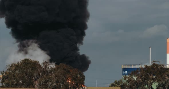 Accident in oil refinery - huge explosions and fireballs rising. Thick black smoke covers the sky. alt