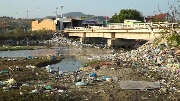 A bridge over a river polluted with plastic trash. Tons of plastic garbage are lying along the river alt
