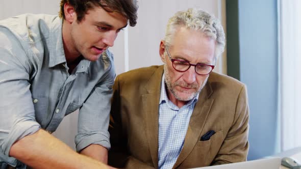 Businessman and coworker discussing over laptop alt