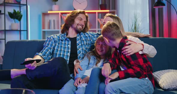 Smiling Loving Parents with Their Two Kids Sitting Together on the Couch in the Evening alt