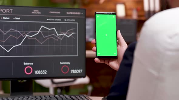 Back View of Caucasian Businessman Holding Mobile Phone with Green Screen alt
