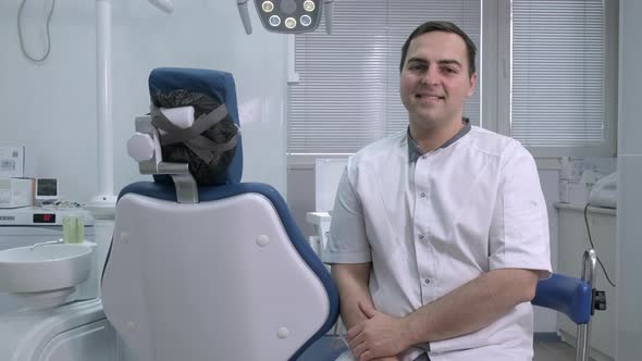 Male Dentist Sitting on Background of Dentists Chair in Dental Office alt