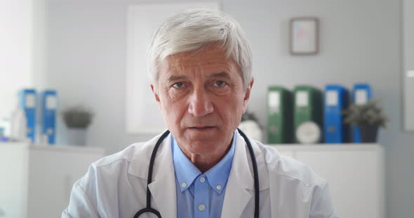 Serious Mature Doctor Wearing White Uniform Coat with Stethoscope Speaking Looking at Camera alt