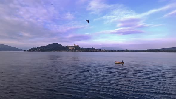 Wide-angle pov of small fishing boat with fisherman rowing in calm lake waters of Maggiore lake in I alt