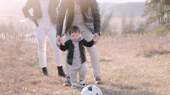 Happy Parents and a Cute Son Are Playing Football Outside alt