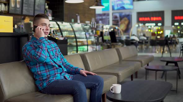 A Young Man Is Sitting in a Cafe and Talking on the Phone. A Man Is Talking on the Phone and alt