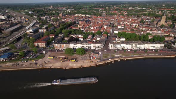 Aerial following of inland shipping large cargo vessel leaving ripple waves on river IJssel passing alt