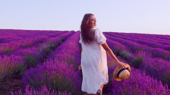 Young Woman in White Dress Walking Through a Lavender Field on Sunset