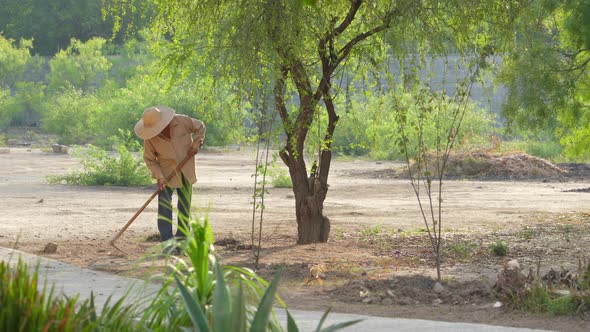 Unrecognizable Man With Hat Working In The Field And Large Garden With Worker Tool alt