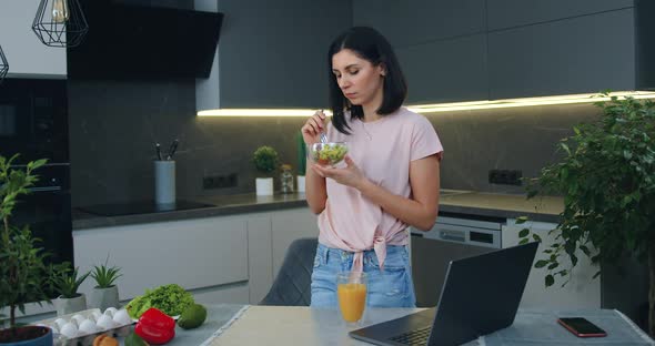 Woman Eating Fresh Vegetable Salad while Standing in Contemporary Kitchen alt