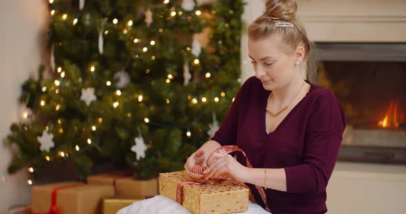 Young Woman Tying Ribbon On Christmas Present alt