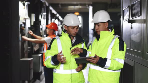 Male Electrical Engineers in Hard Hats Discuss New Project while Using Tablet Computer