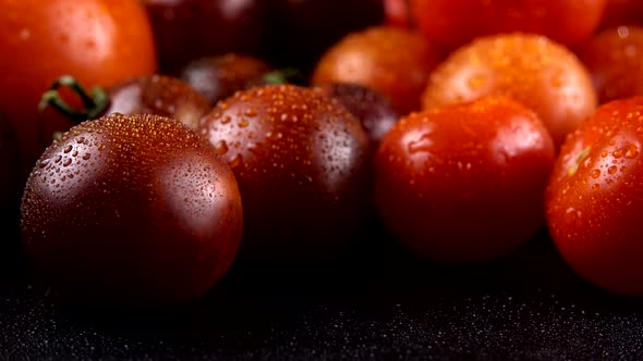 Cherry tomatoes on a black background in water drops. alt