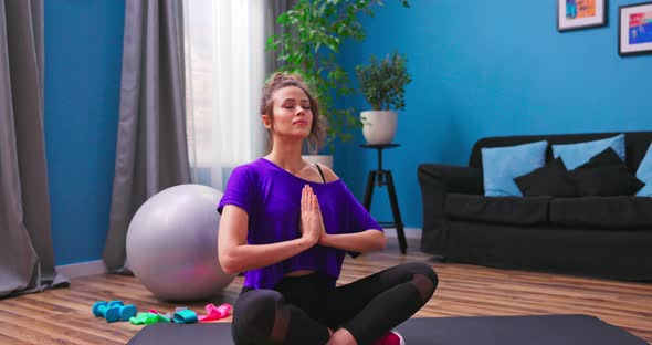 Portrait of Beautiful Young Woman Dressed in Fitness Clothes Meditates While Sitting in Lotus alt